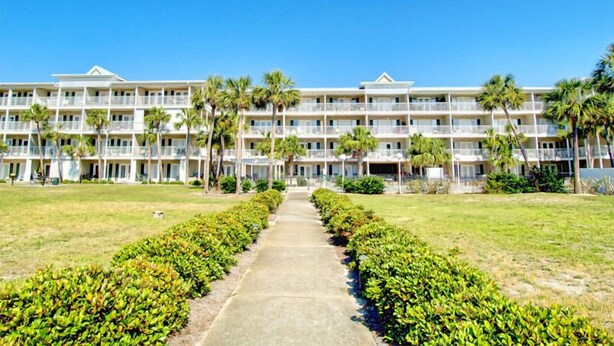 A multi-story hotel with a central courtyard, palm trees, and a clear blue sky. - Grand Caribbean by Southern (Pensacola)