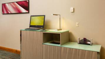 A hotel desk with a laptop, a lamp, and a small shelf with a book holder.