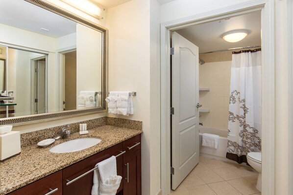 A bathroom with a granite countertop sink, a large mirror, and a shower with a floral curtain.