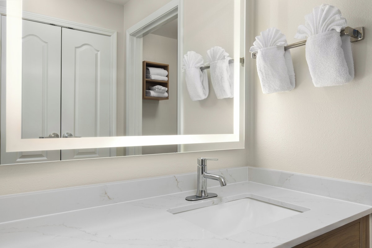 A bathroom with a large mirror, a sink, and towels hanging on a rack.