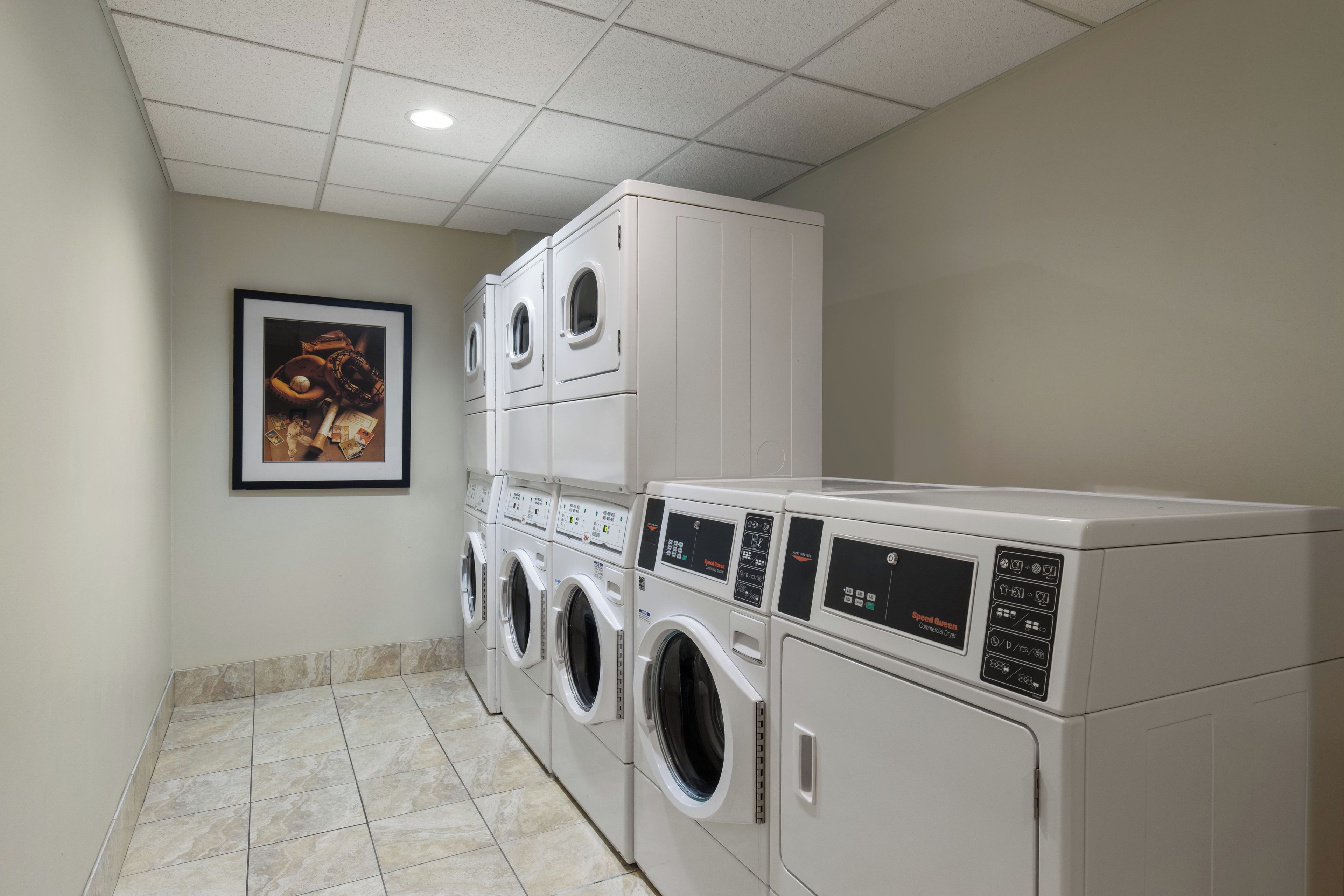 A laundry room with stacked front-loading washers and dryers, a tiled floor, and a framed picture on the wall.