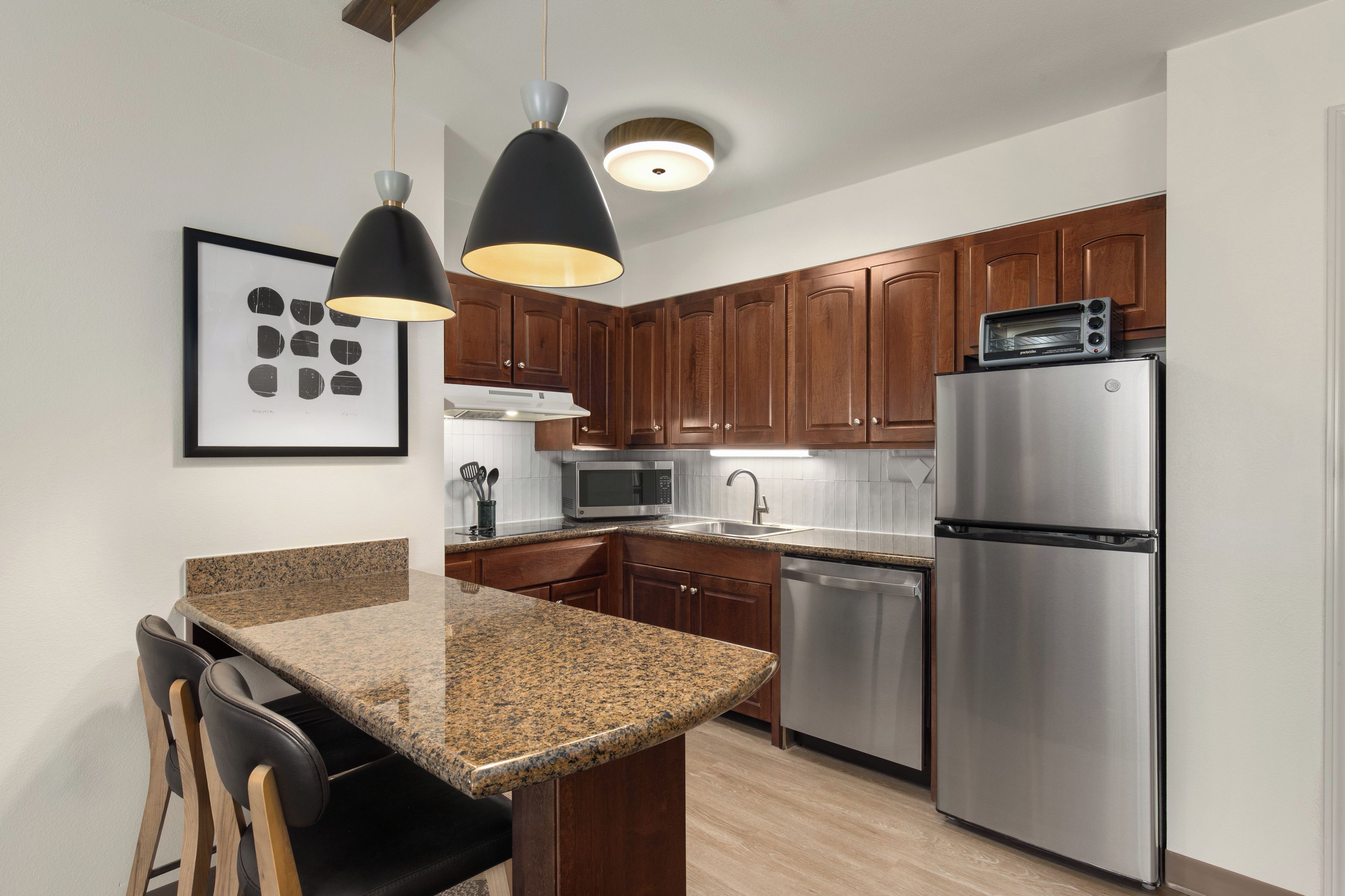 A modern kitchen with granite countertops, stainless steel appliances, wooden cabinets, and pendant lighting.