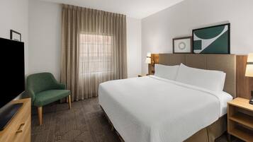 A hotel room with a large bed, a television, a chair, a desk, and a window with curtains.