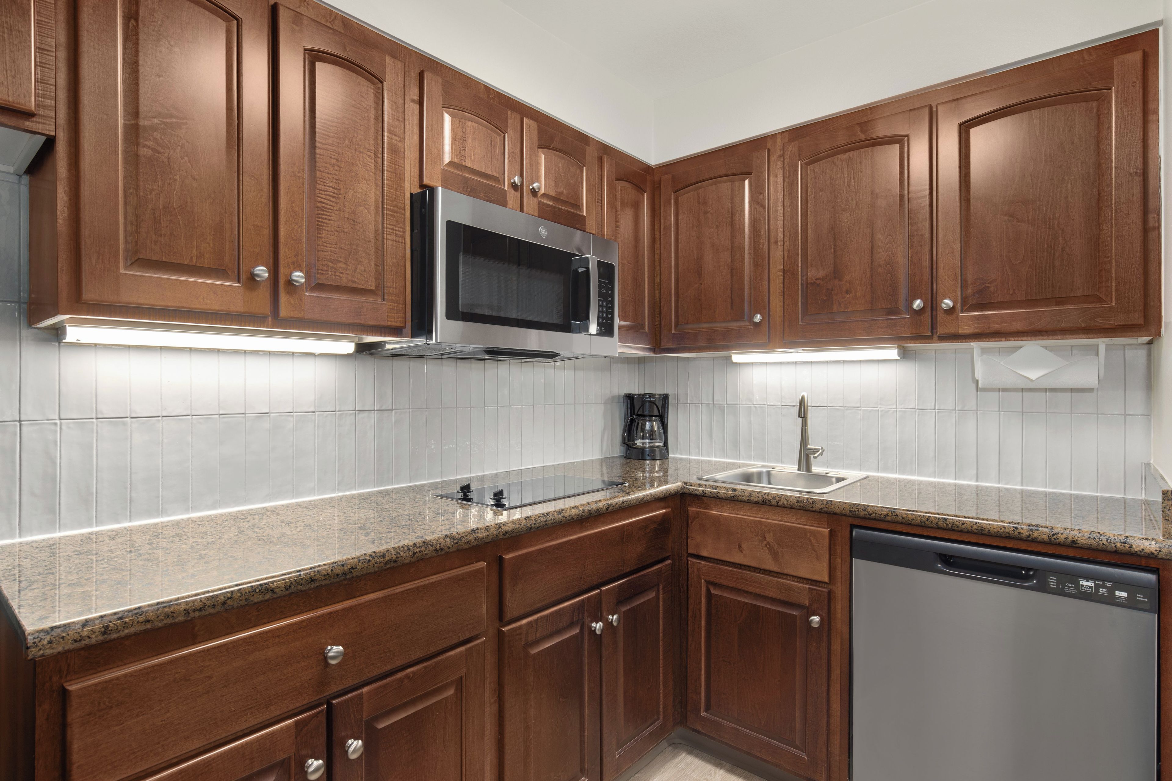 A kitchen with wooden cabinets, a stainless steel microwave, a coffee maker, and a dishwasher.