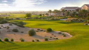 A golf course with sand bunkers, palm trees, and a large building with multiple windows and a balcony. - Arabian Ranches Golf Club (Dubai)