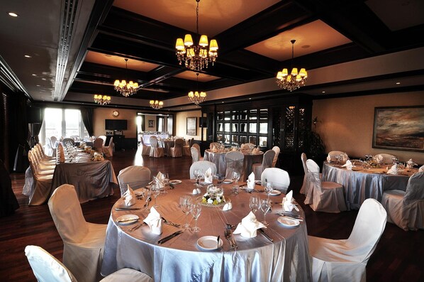 A banquet hall with round tables set for dining, chandeliers, and a large window.