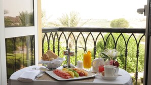 A breakfast table with a variety of fruits, a glass of orange juice, and a cup on a balcony overlooking a garden. - Arabian Ranches Golf Club (Dubai)