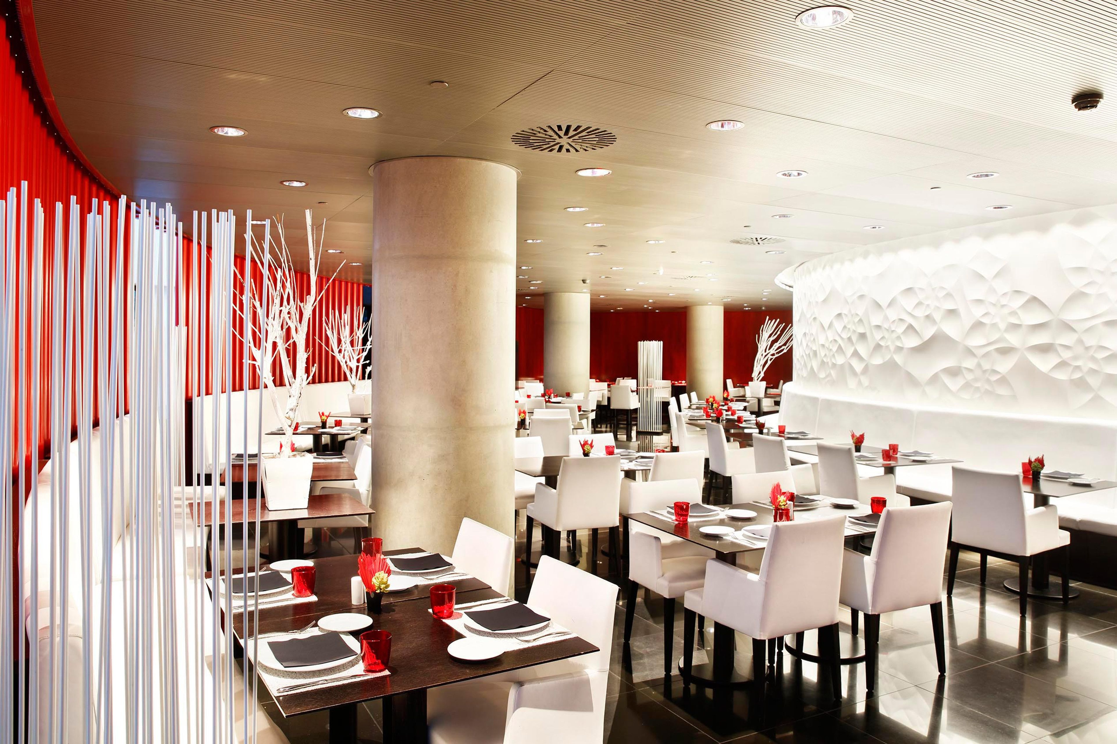 Een modern restaurant met witte stoelen en tafels, rode accenten en een opvallend plafondontwerp.