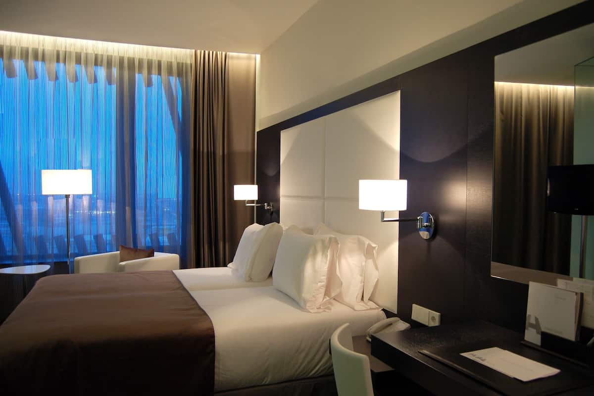 Habitación de hotel con una cama grande, dos lámparas de noche, un escritorio con una silla y un espejo amplio.