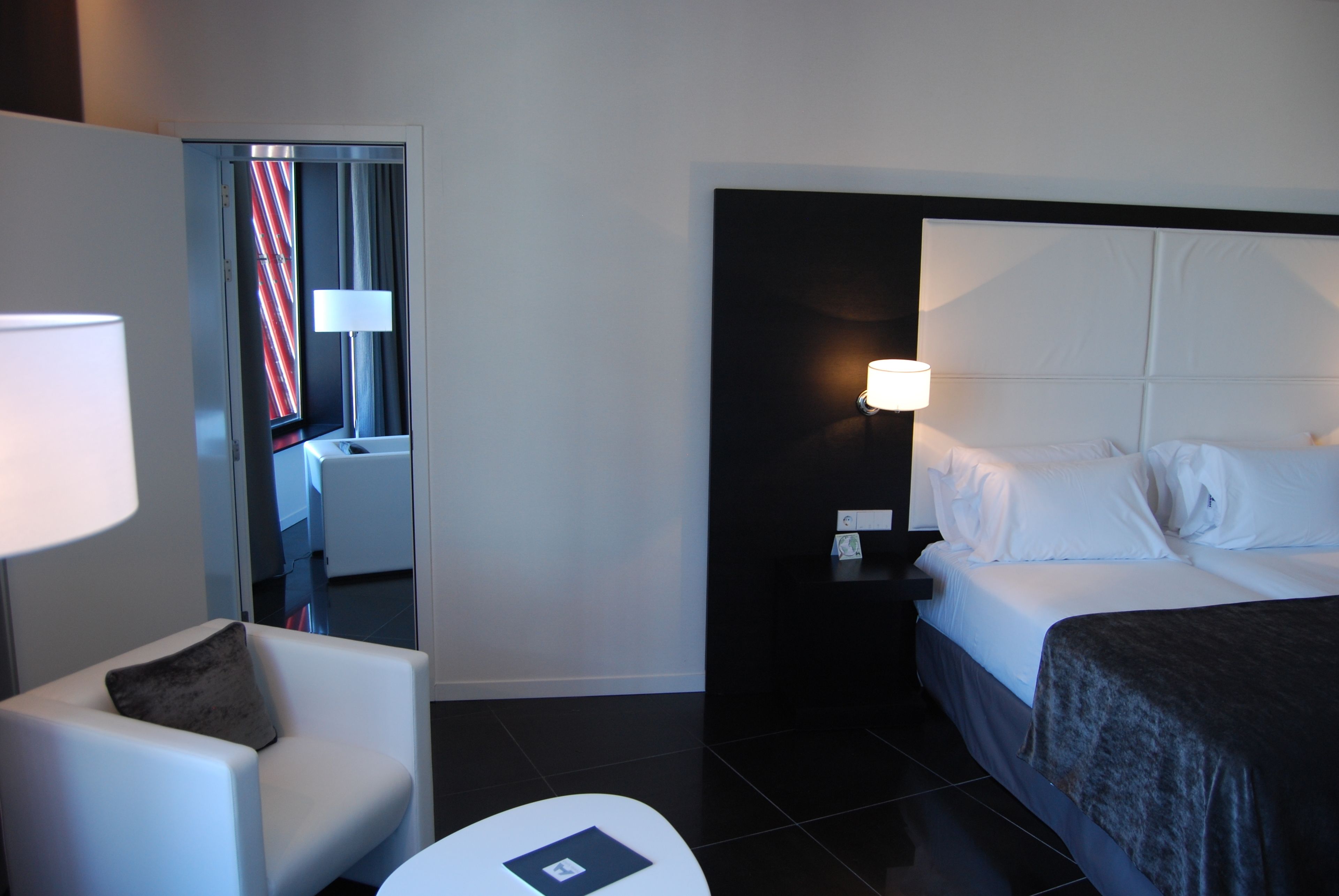 Una habitación de hotel con una cama, una silla, una mesita de noche y una lámpara.