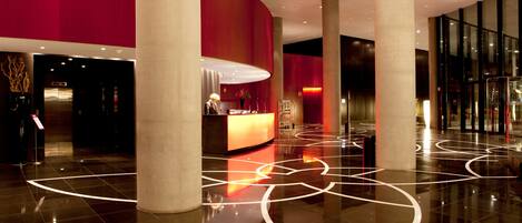 A modern lobby with a reception desk, large pillars, and a polished floor with geometric patterns.