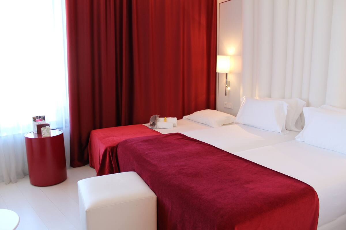 Una habitación de hotel con una cama grande, una pared de acento roja y una mesita de noche pequeña.