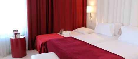 A hotel room with a large bed, a red accent wall, and a small side table.