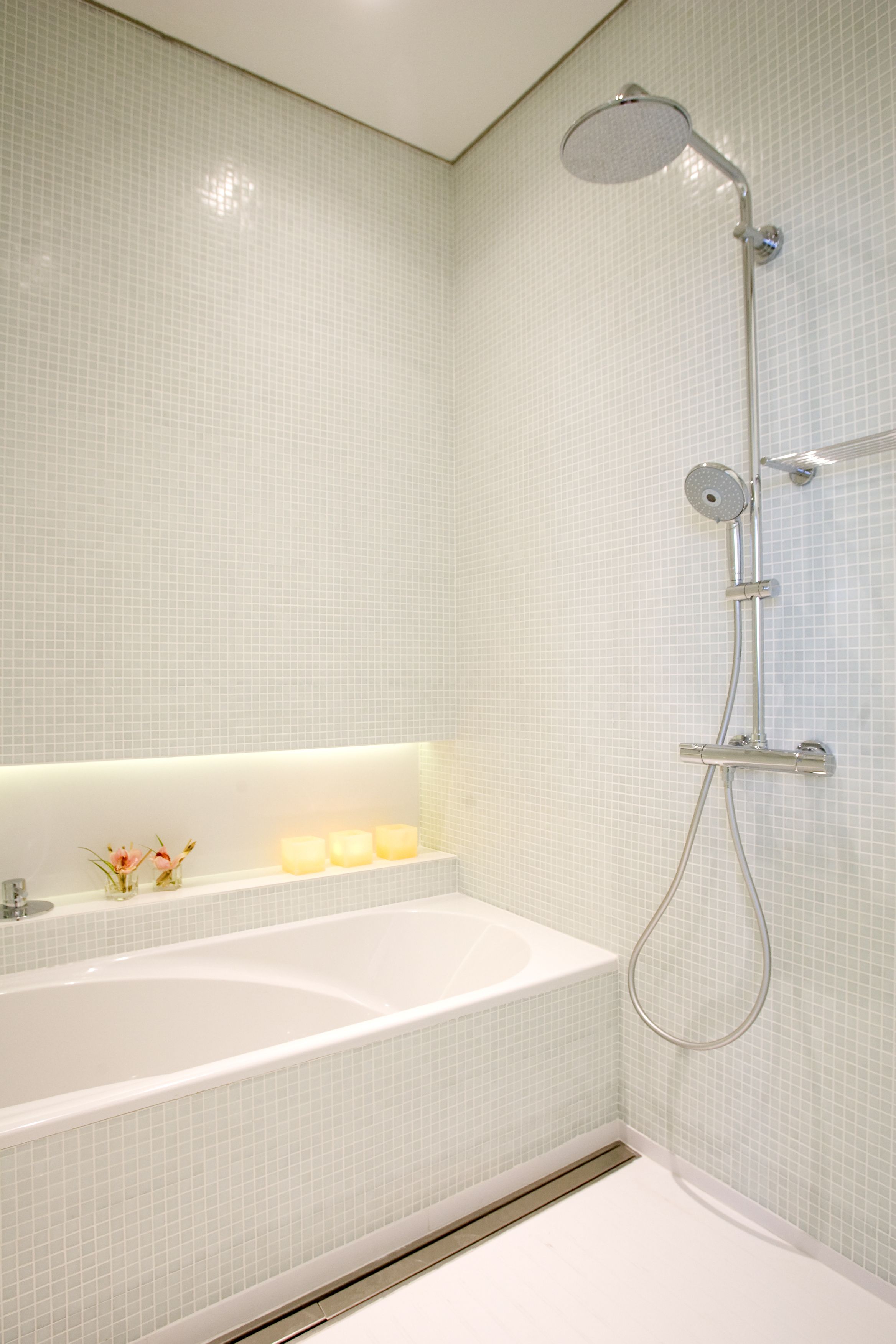A bathroom with a white bathtub, a showerhead, and a tiled wall.