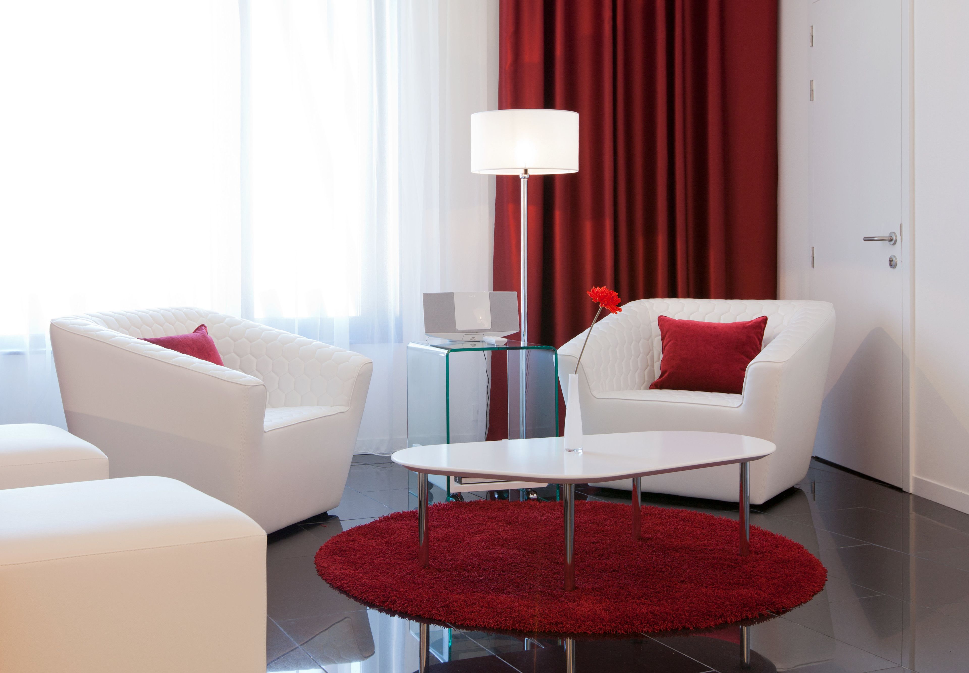 A modern living room with white sofas, a round coffee table, and a red rug.