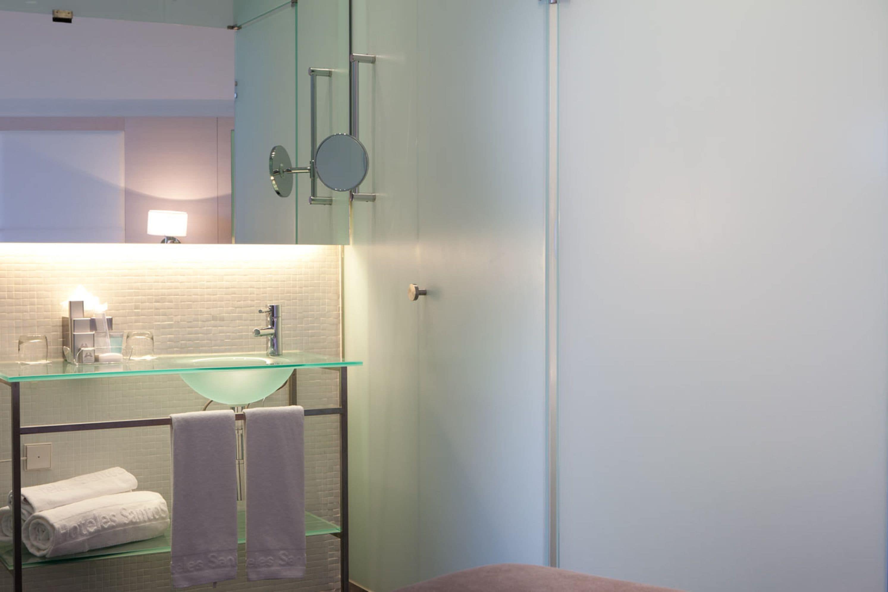 Un baño moderno con un lavabo de vidrio, un espejo y dos toallas en un estante.