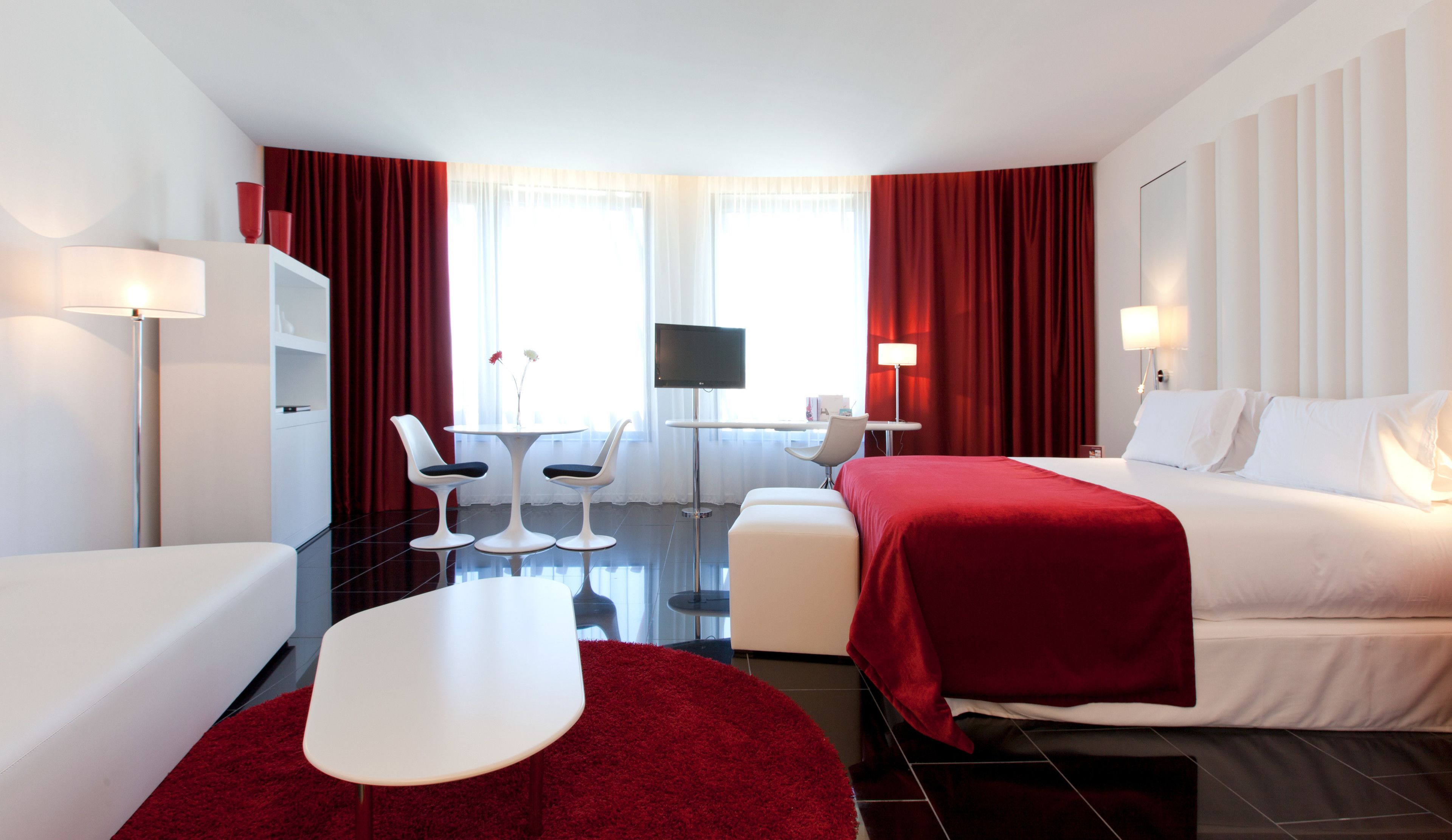 Una habitación de hotel moderna con cama, escritorio, dos sillas, televisor y alfombra roja.