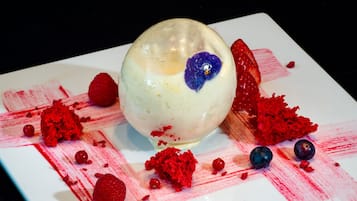 Un postre con base blanca esférica, una rodaja de fresa y frambuesas y arándanos esparcidos.