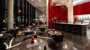 Un restaurante moderno con mesas redondas y sillas negras, una zona de bar y grandes ventanales.