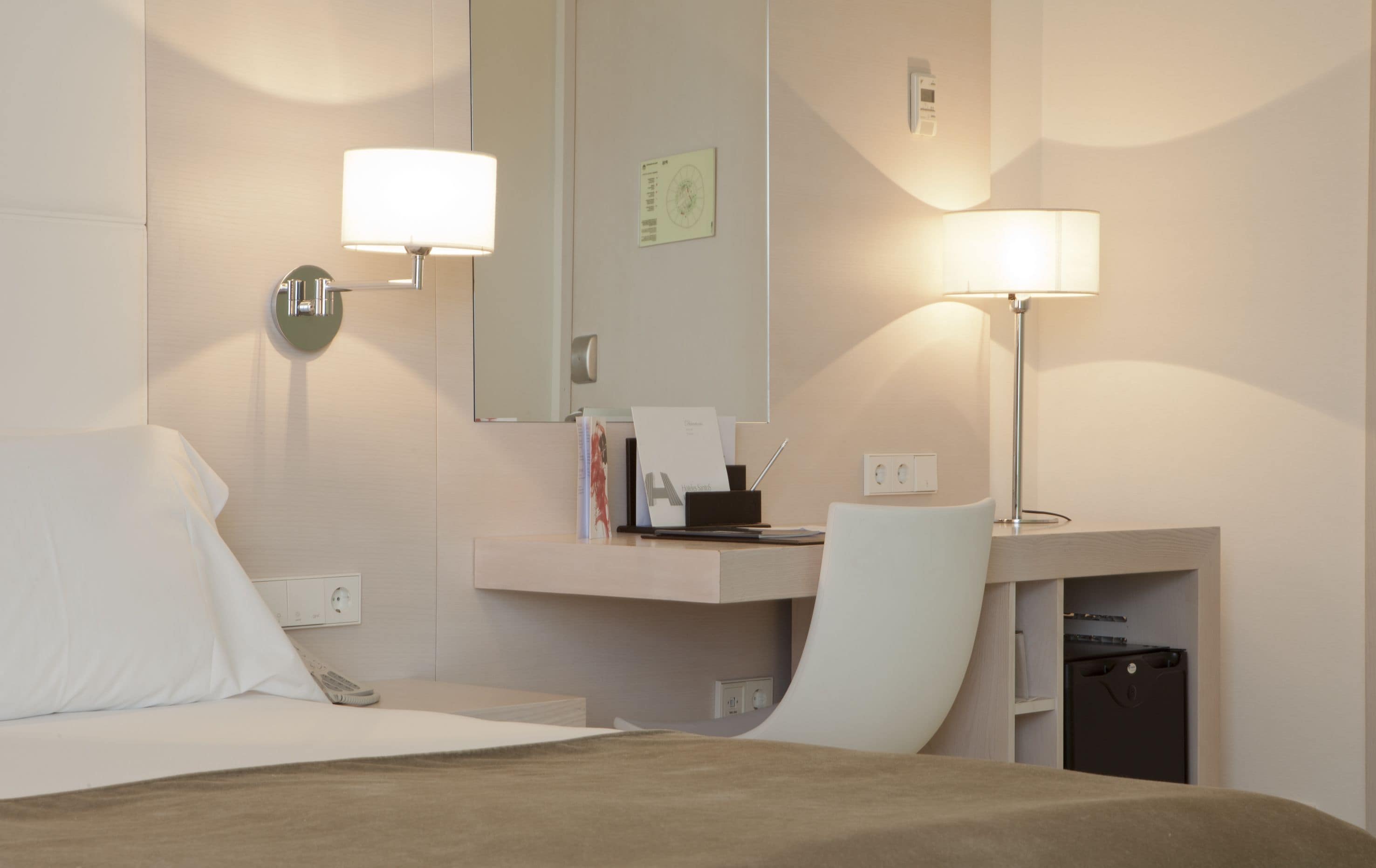 Une chambre d’hôtel avec un lit, un bureau doté d’une lampe, une chaise et un miroir.