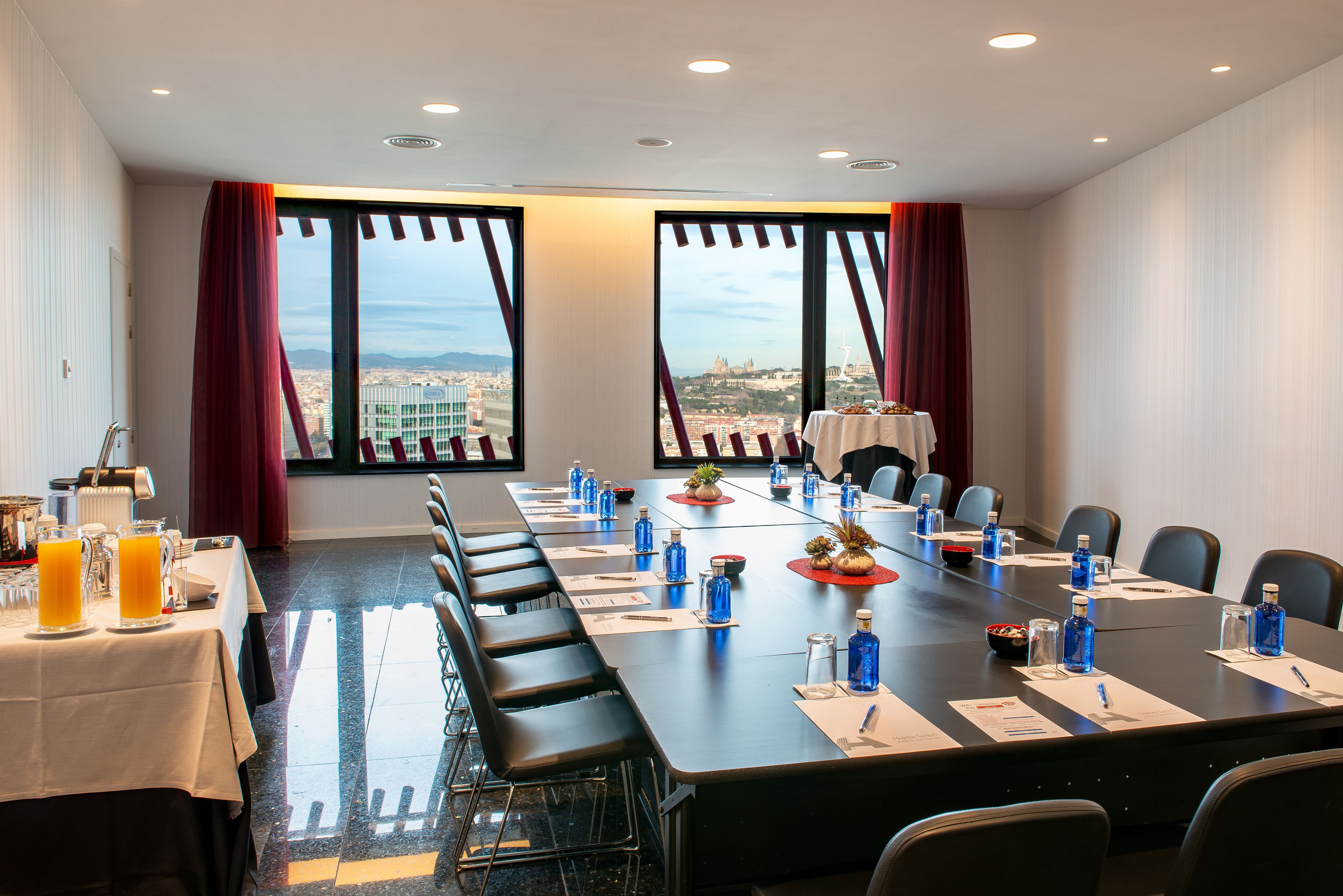 A conference room with a long table, chairs, and a city view through large windows.