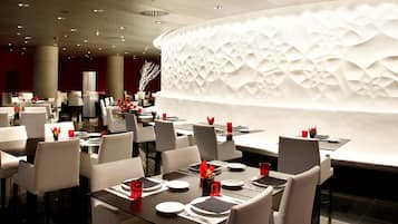 Un restaurante moderno con mesas y sillas blancas, servilletas rojas y un diseño de pared texturizado único.
