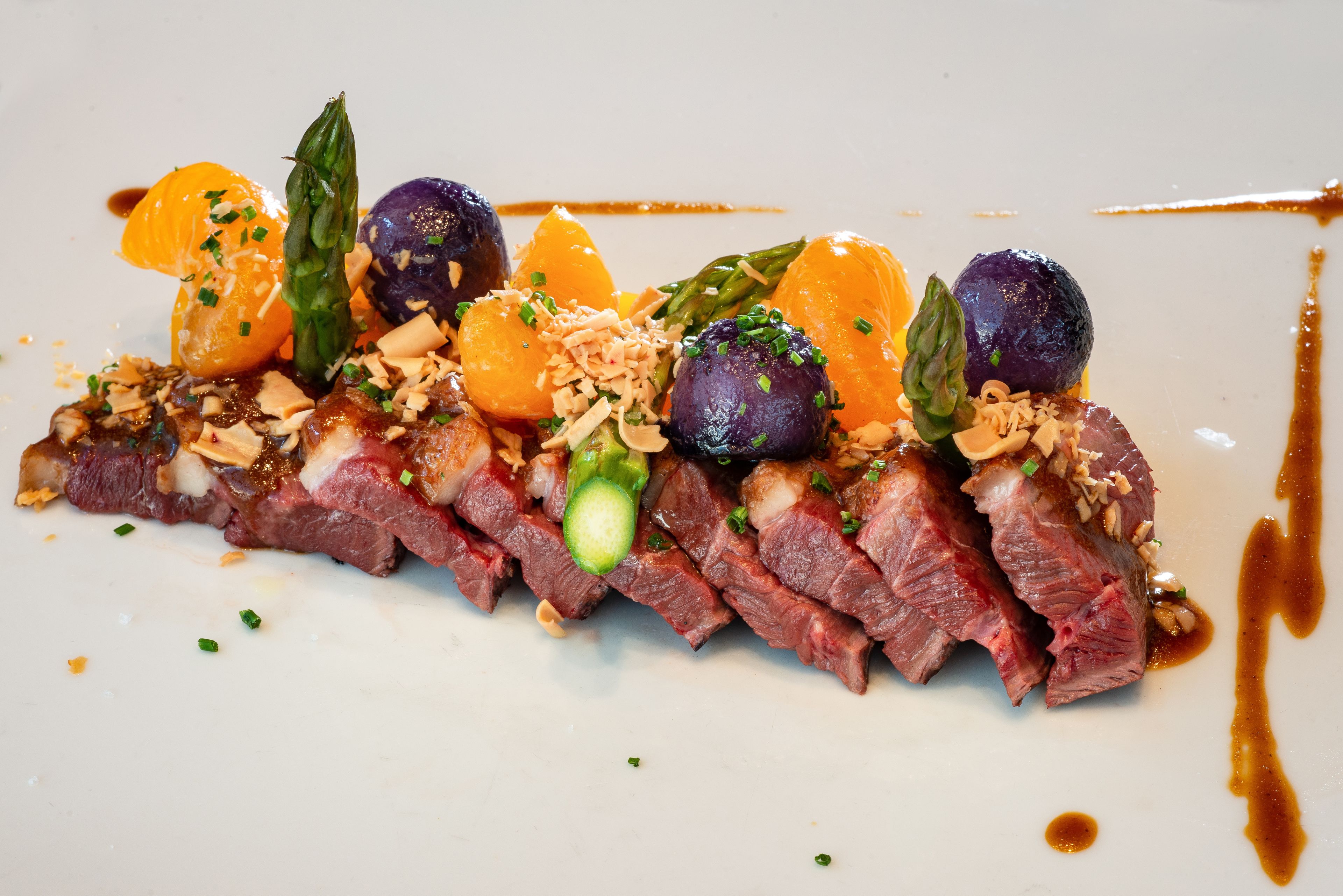 A dish with sliced meat, vegetables, and garnishes on a white plate.