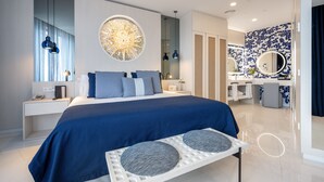 Una habitación de hotel moderna con una cama grande, una mesita de noche, un escritorio, un espejo y un baño con lavamanos y espejo.