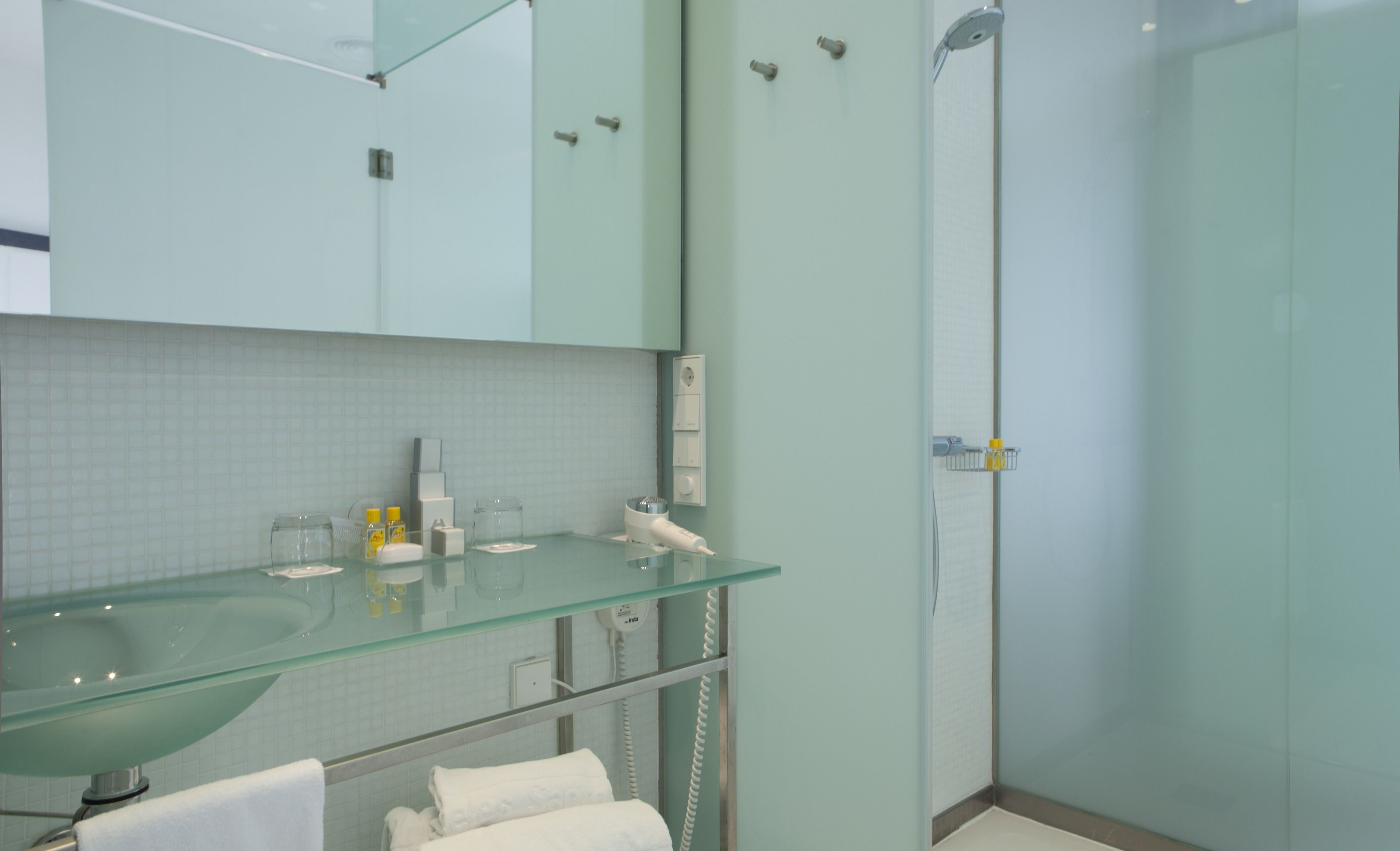 A modern bathroom with a glass sink, a mirror, a towel rack, and a shower area.