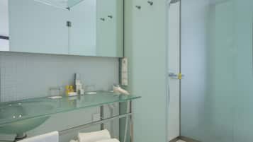 A modern bathroom with a glass sink, a mirror, a towel rack, and a shower area.