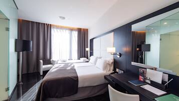 Ein Hotelzimmer mit zwei Betten, einem Schreibtisch, einem Stuhl, einem Flachbildfernseher und einem großen Spiegel.