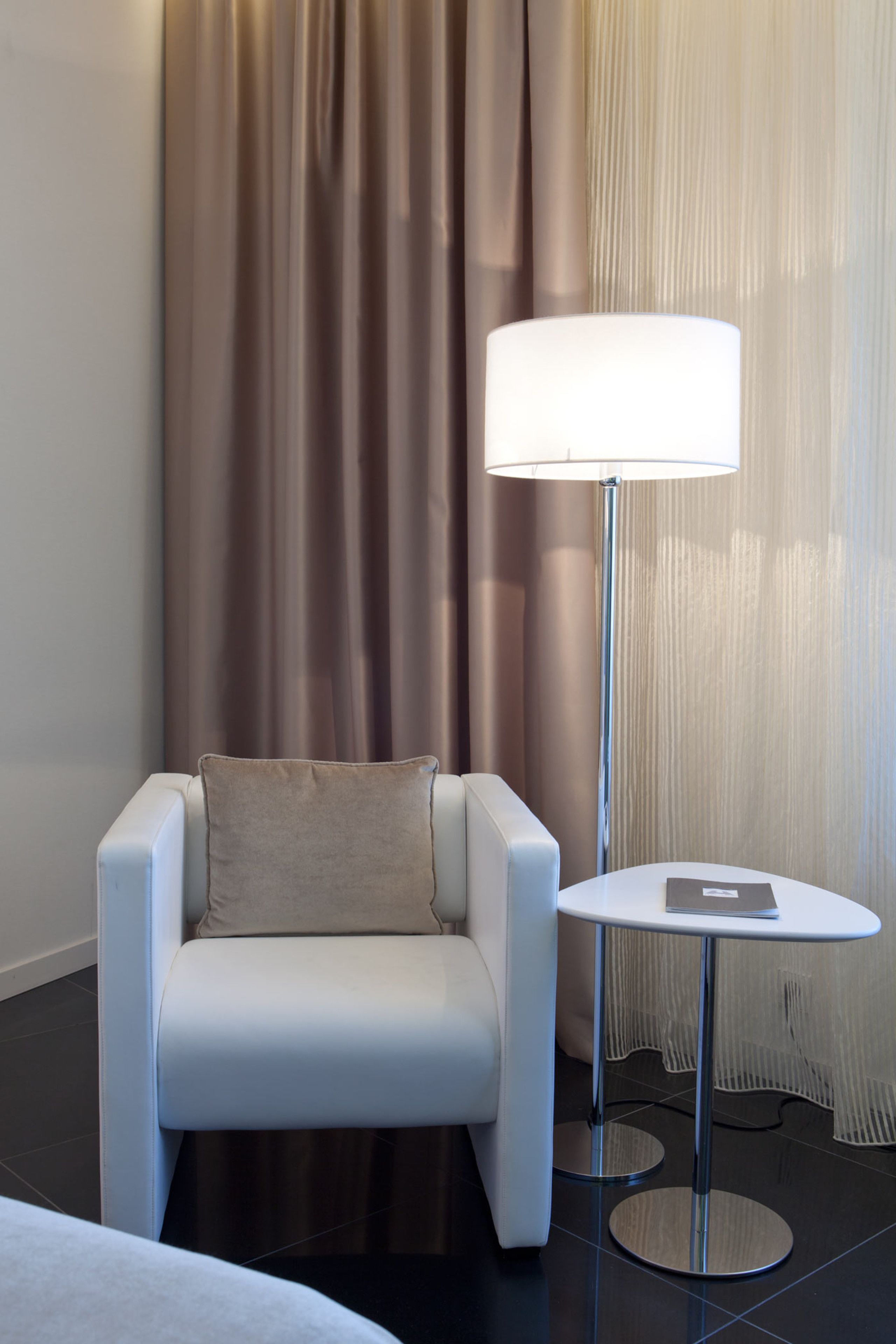 A modern hotel room with a white armchair, a small round table, and a floor lamp.