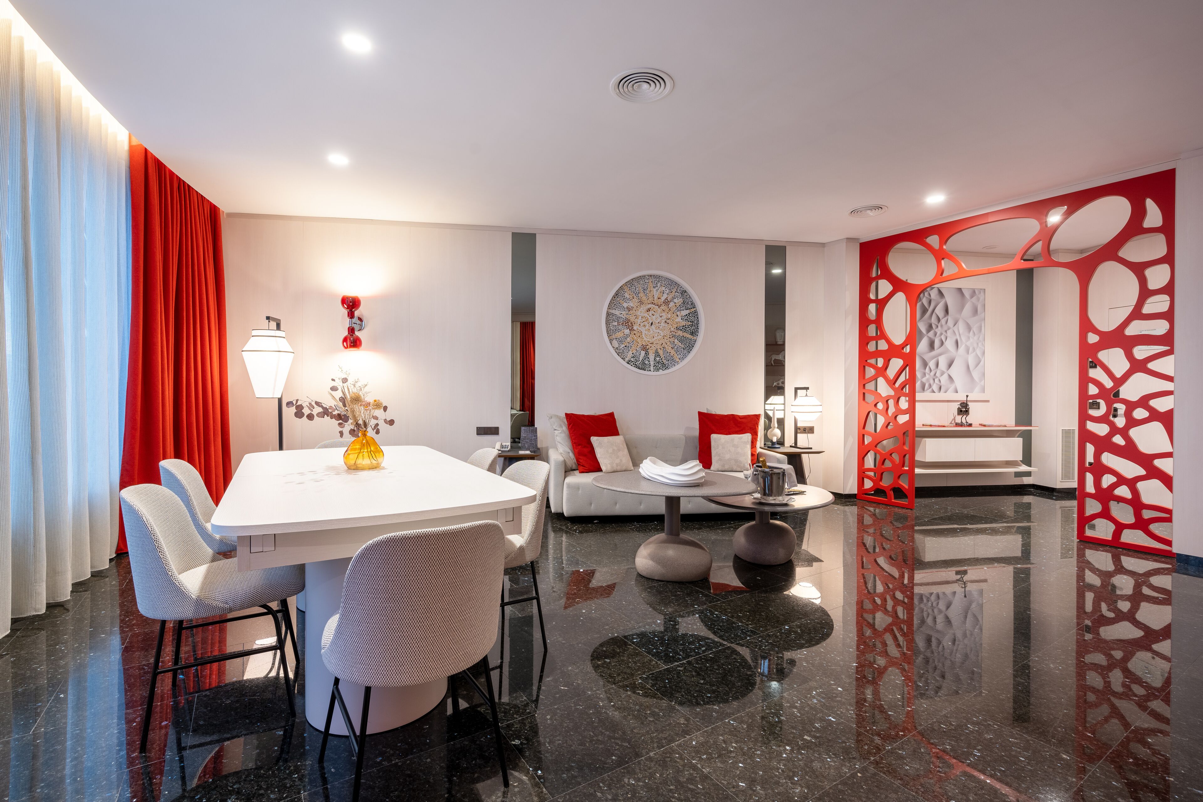 A modern dining area with a white table, grey chairs, and a red accent wall.