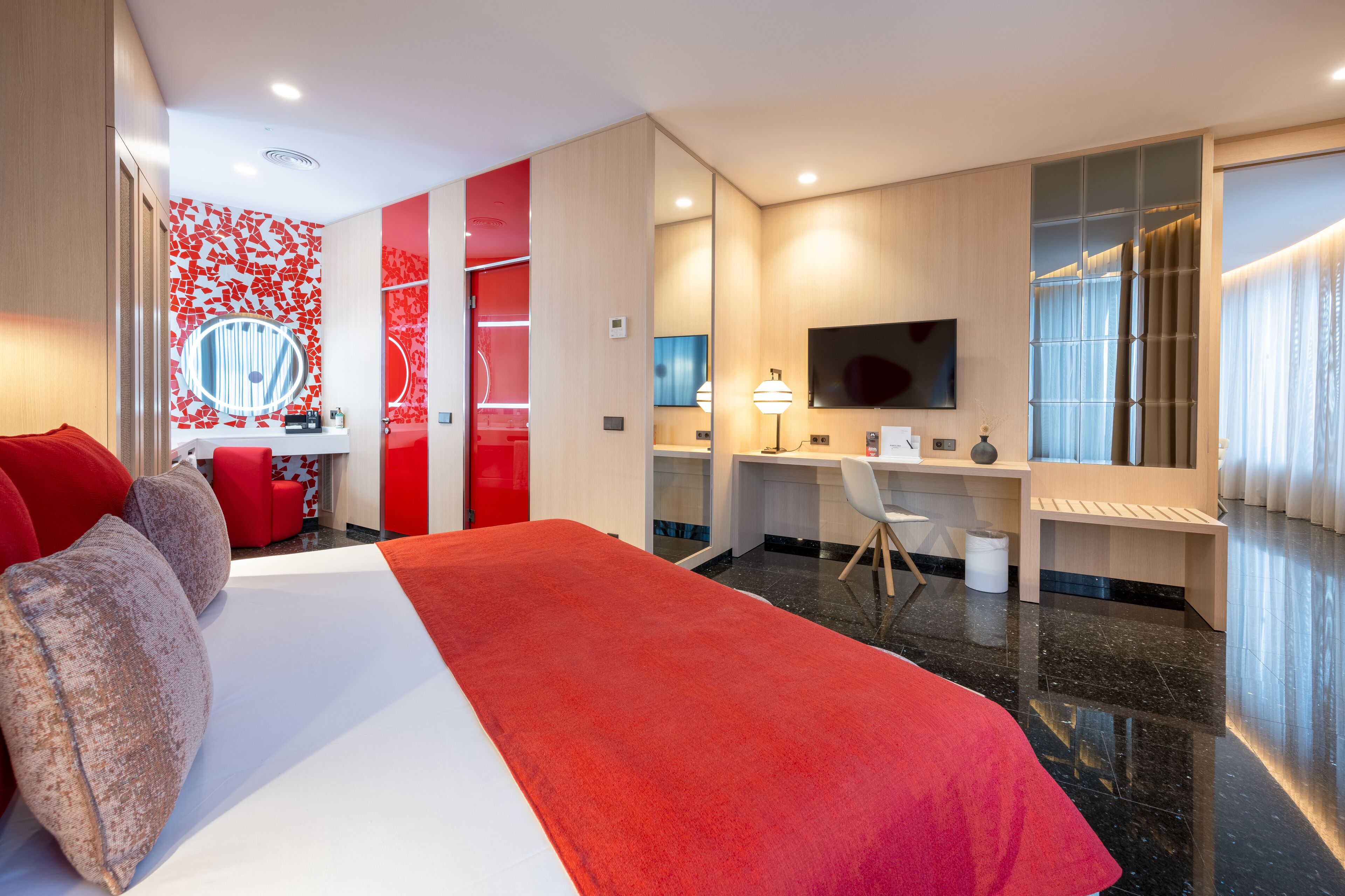 Habitación de hotel moderna con una cama grande, un escritorio, un televisor y una pared de acento roja.