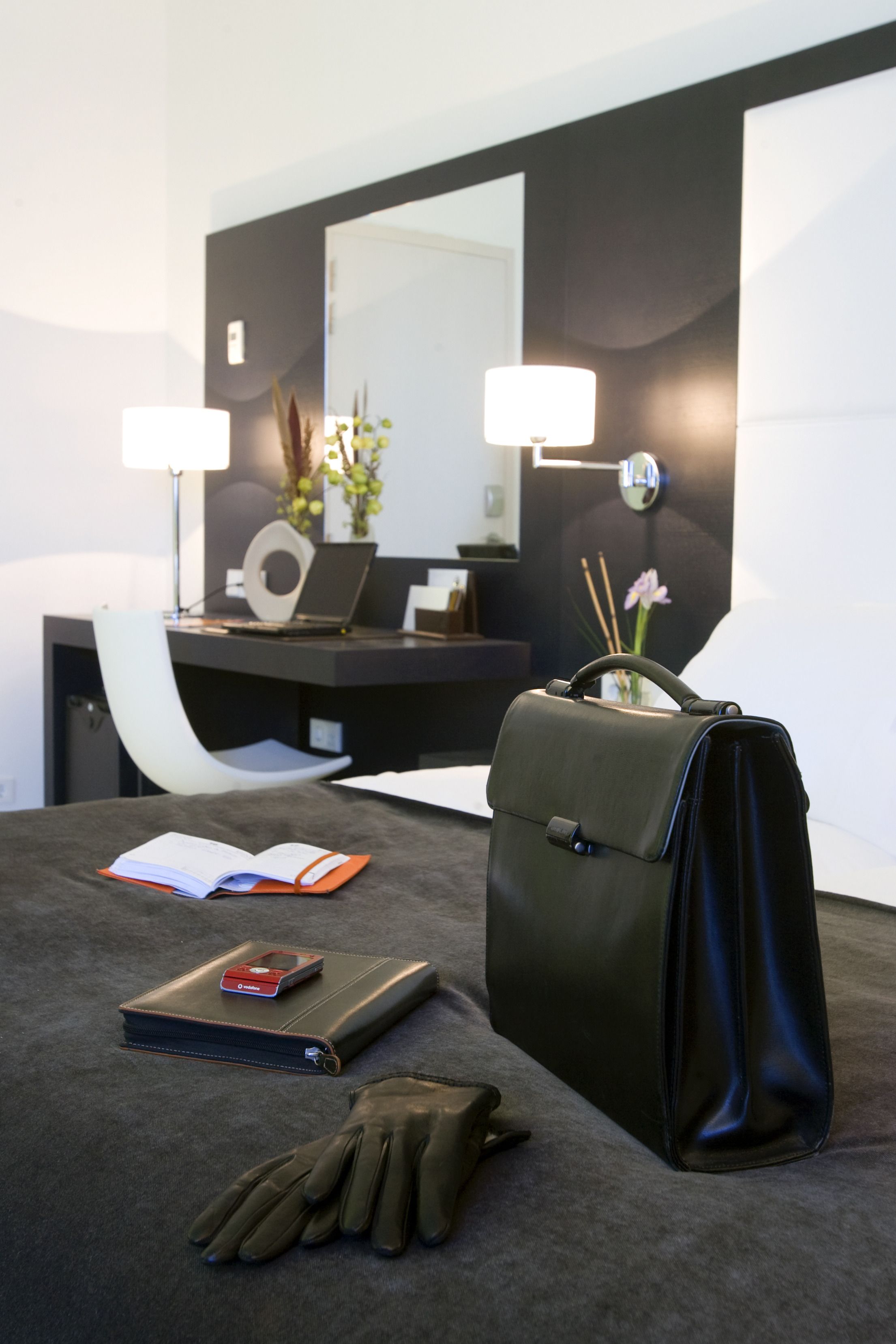 Et pænt hotelværelse med seng, skrivebord med en bærbar computer, lampe og en håndtaske.