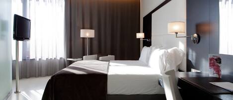 Una habitación de hotel con una cama grande, dos mesitas de noche, un televisor de pantalla plana y un escritorio con una silla.