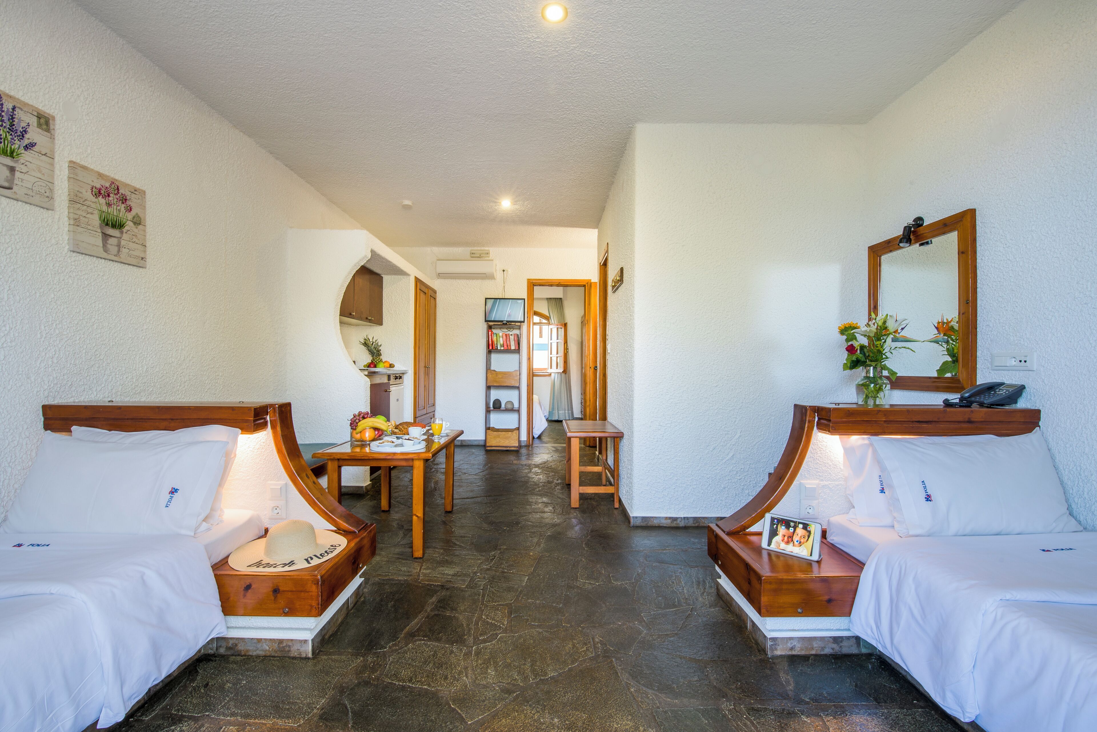 A hotel room with two beds, a small table, a chair, a mirror, and a hallway leading to a bathroom.
