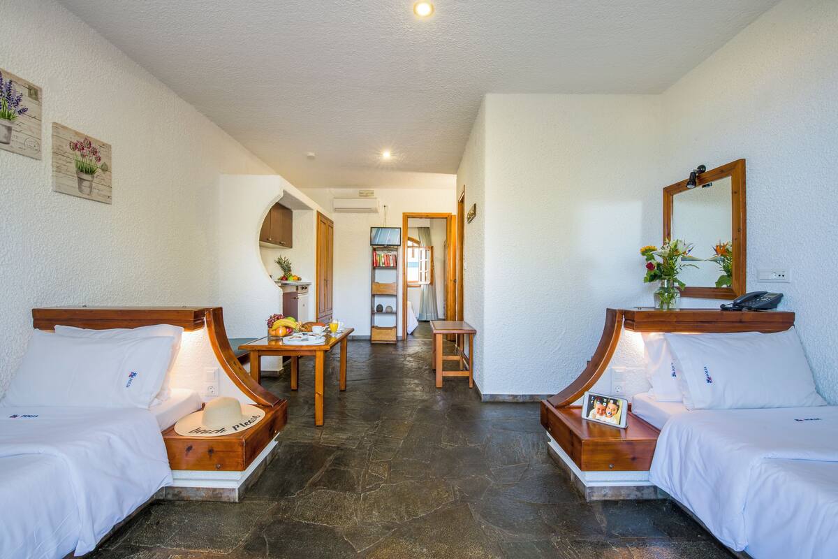 A hotel room with two beds, a small table, a chair, a mirror, and a hallway leading to a bathroom.