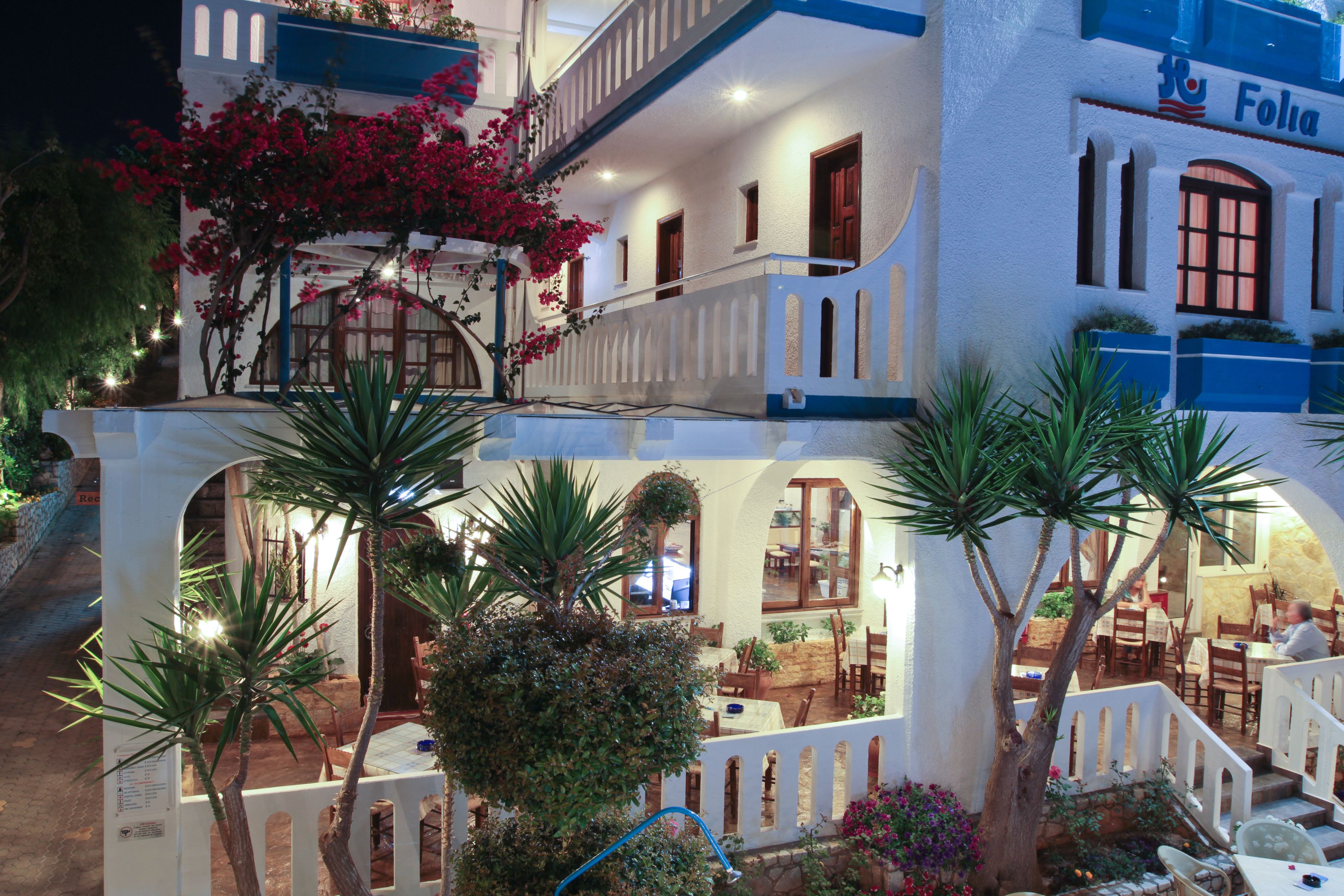A hotel with a white facade, blue accents, and a balcony with red flowers.