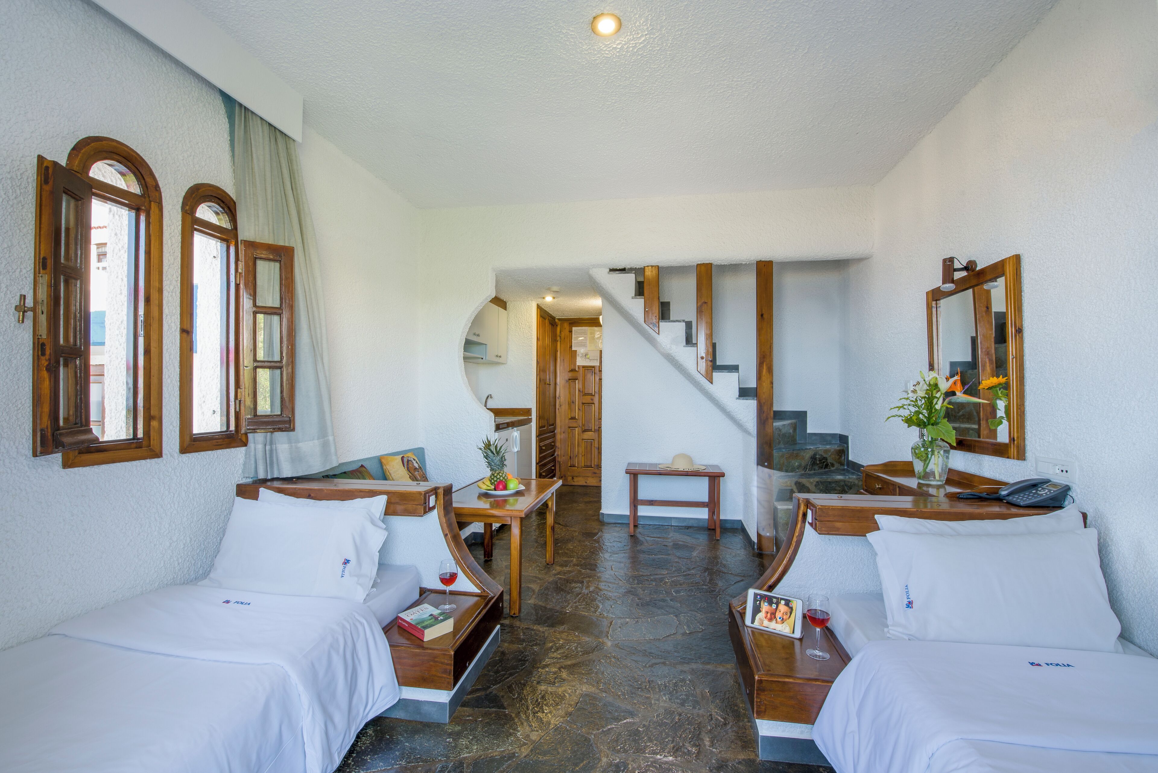 A hotel room with two beds, a wooden staircase, a dining area, and a view of the outside.