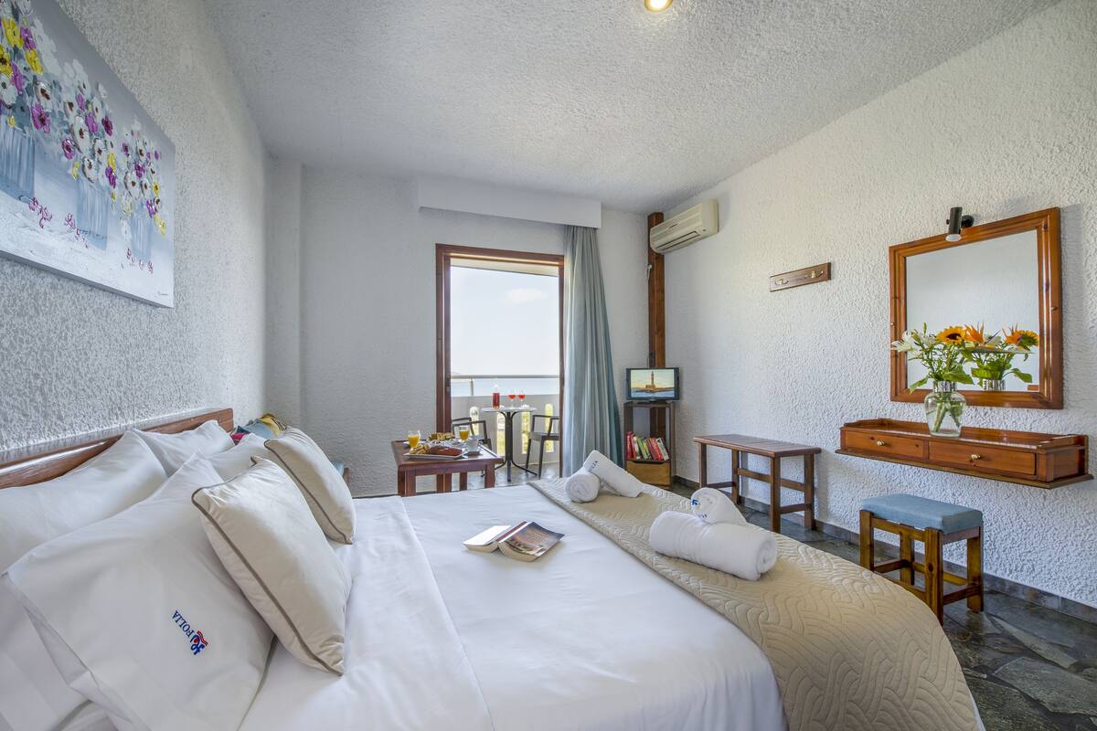 A hotel room with a large bed, a desk, a chair, a small table, a mirror, and a window with a view.