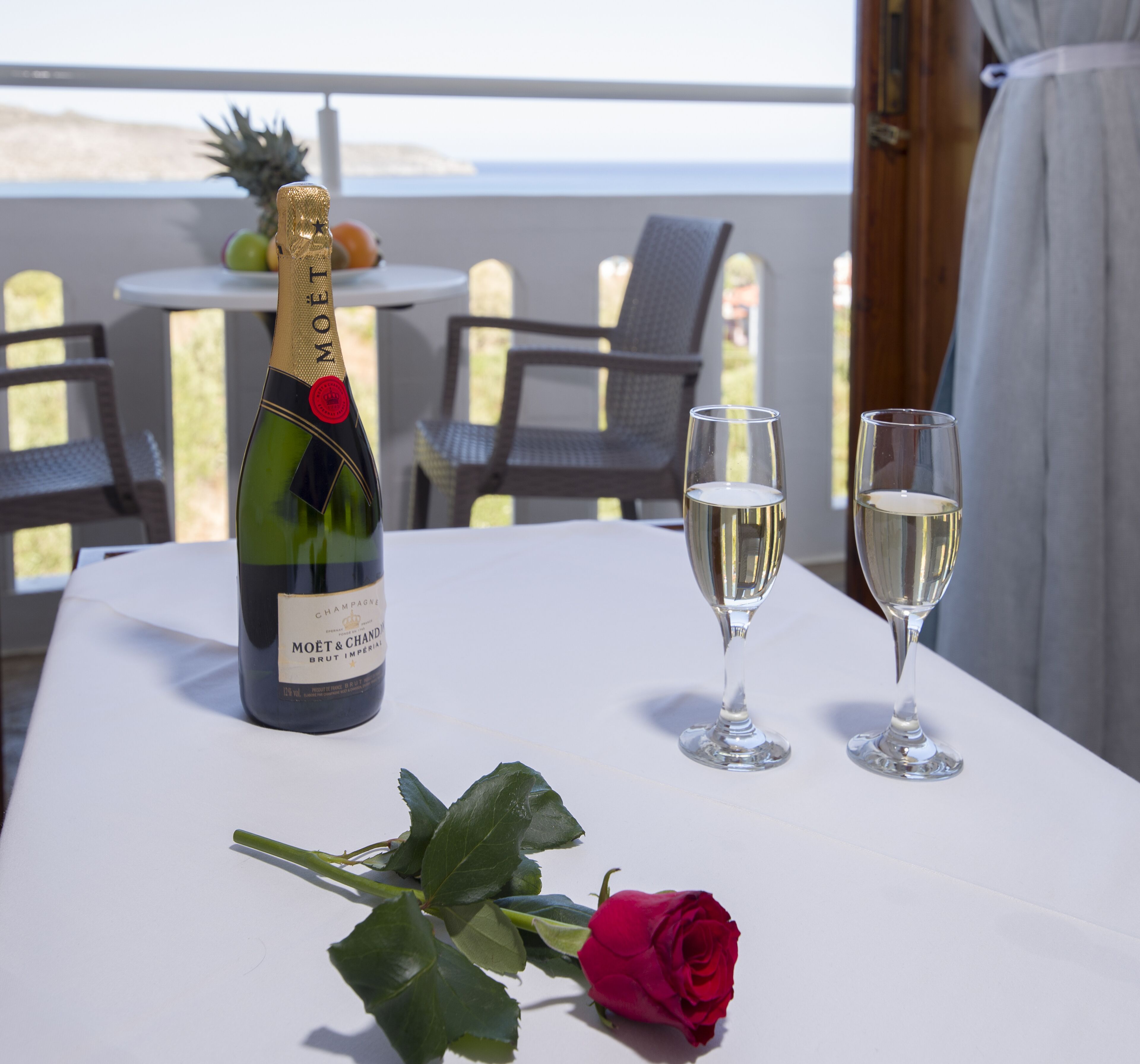 A table with a bottle of champagne, two glasses, and a rose.
