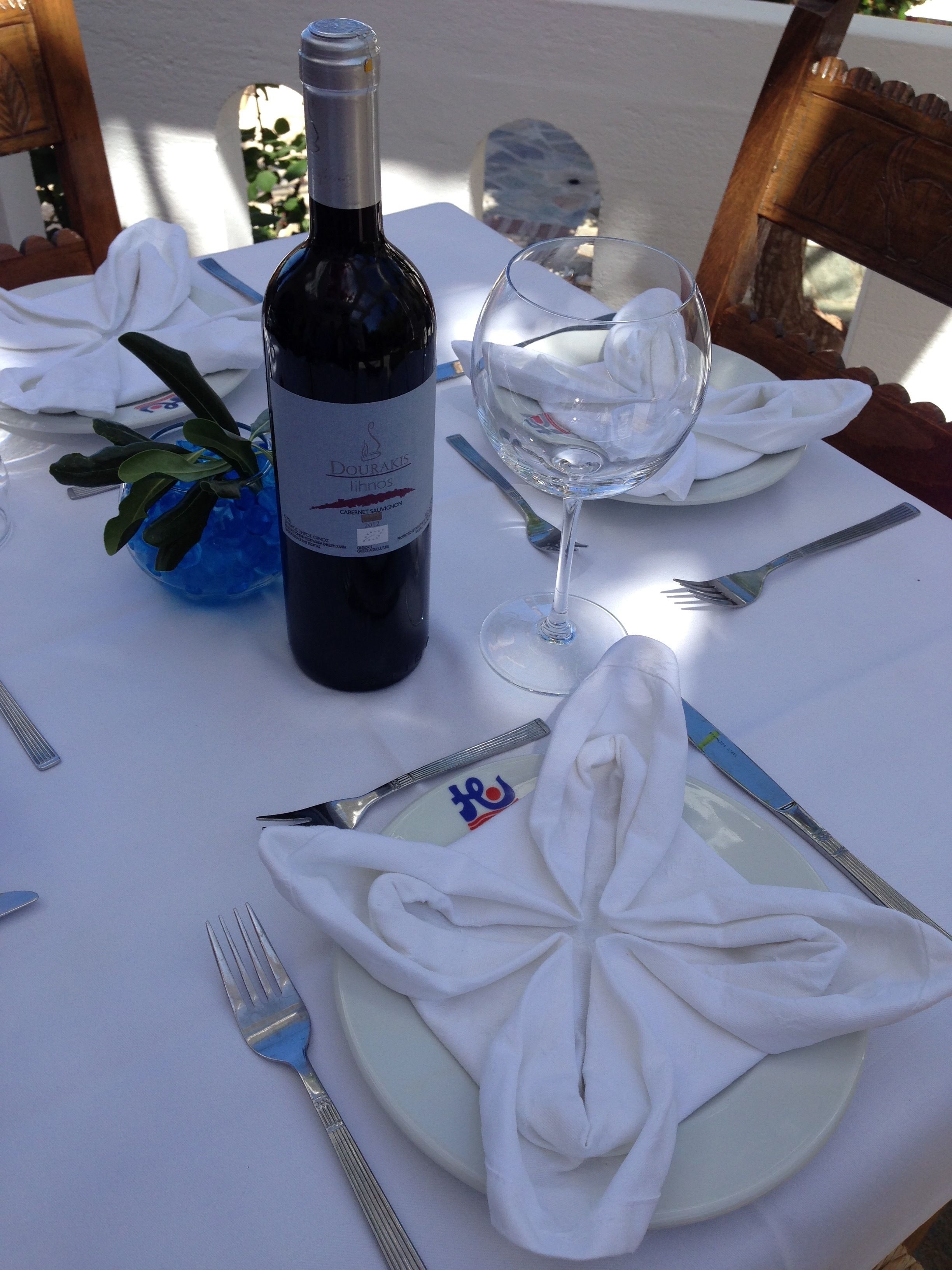 Een gedekte tafel voor een maaltijd, met een fles wijn, een glas en netjes gevouwen servetten.