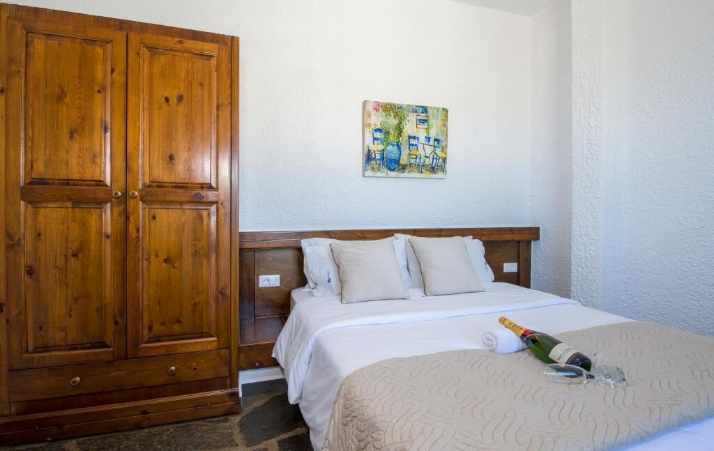 A bedroom with a wooden wardrobe, a bed with white bedding, a painting on the wall, and a bottle of champagne on the bed.