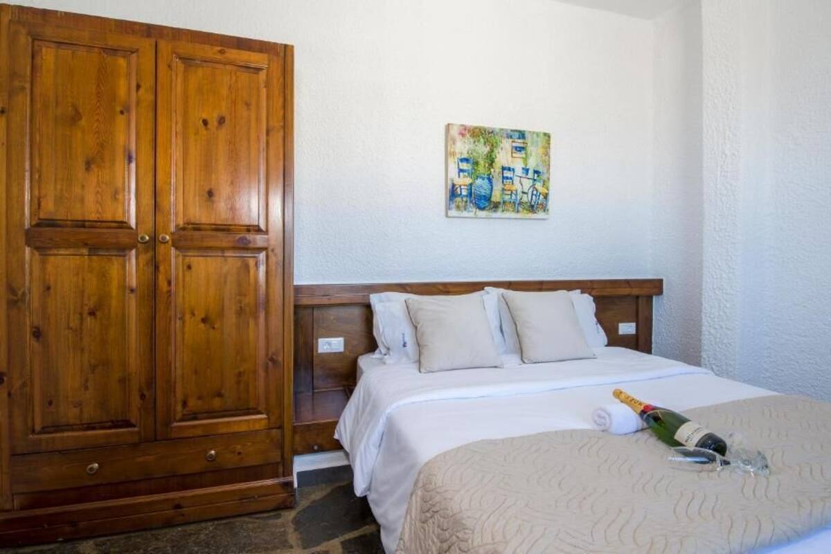 A bedroom with a wooden wardrobe, a bed with white bedding, a painting on the wall, and a bottle of champagne on the bed.