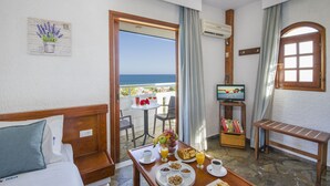 A hotel room with a balcony, a bed, a dining table with breakfast, a TV, and a view of the sea. - Folia Apartments (Chania)