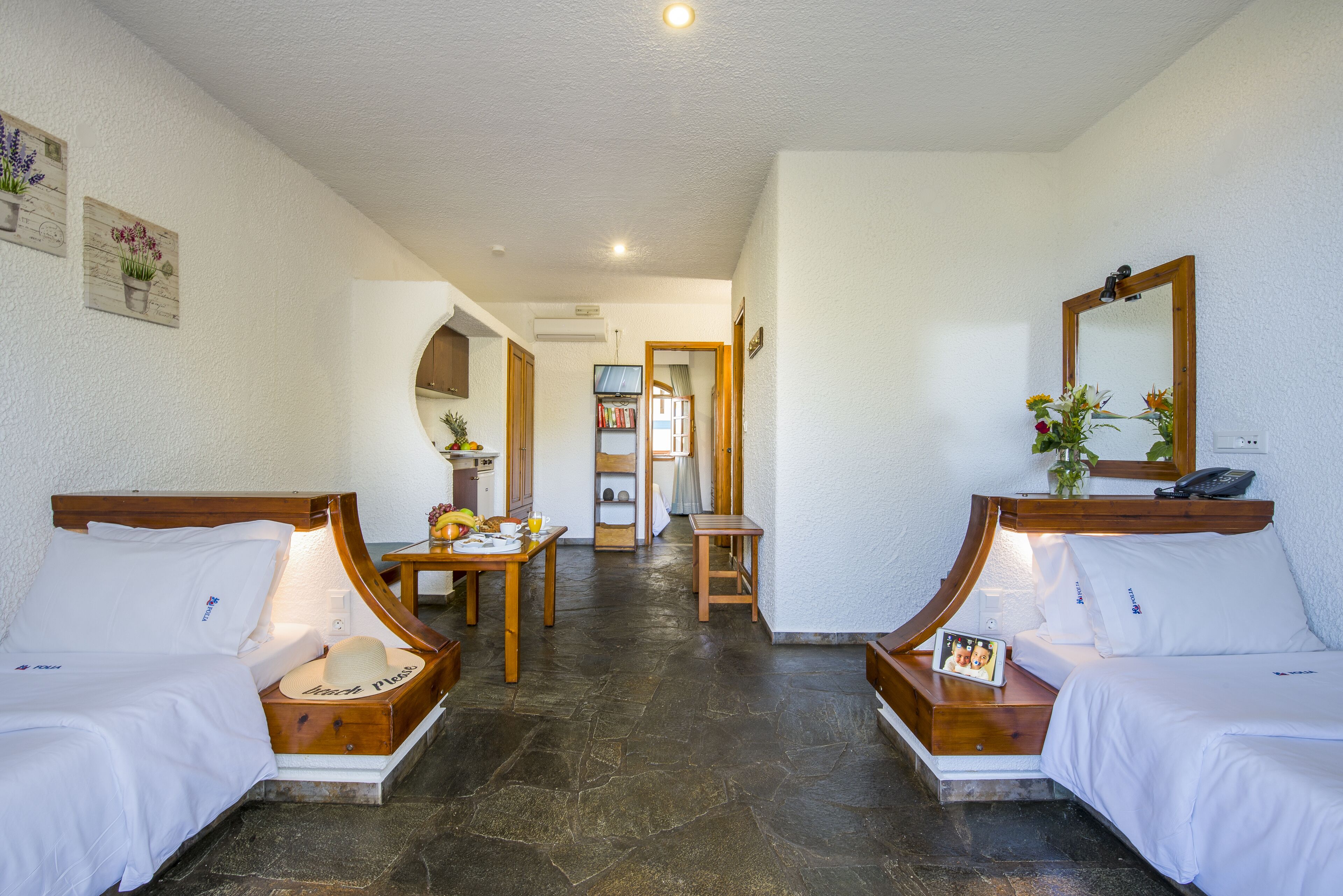 Una camera d'albergo con due letti, un tavolino, uno specchio e un corridoio che conduce al bagno.