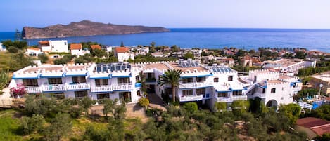 A coastal resort with white buildings featuring blue accents, a view of the sea, and a distant mountain.