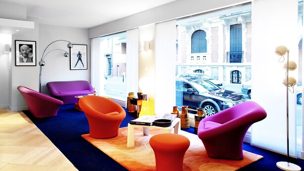 Un salon moderne avec des fauteuils aux couleurs vives, une table basse et une grande fenêtre donnant sur la ville.