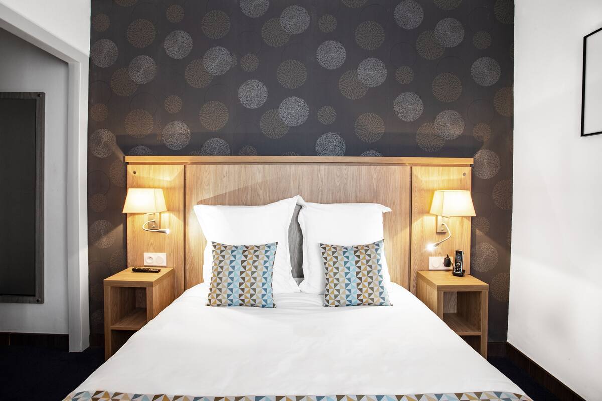Une chambre d’hôtel avec un grand lit, deux tables de chevet avec des lampes et un papier peint à motifs.